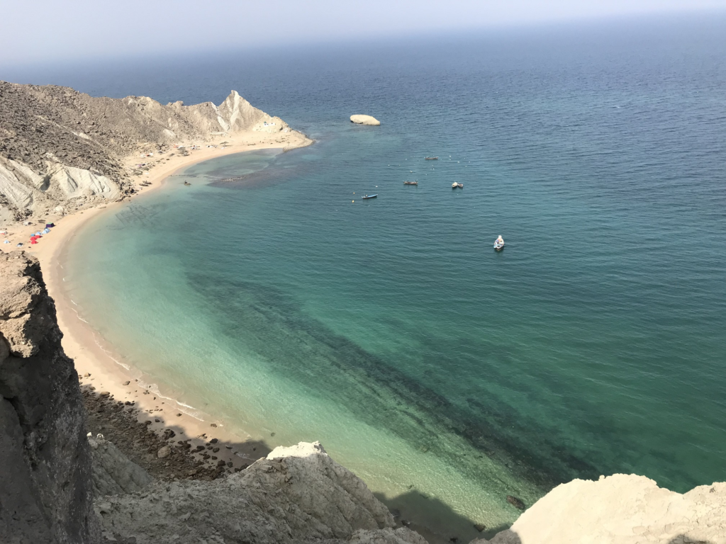 A scenic view of a secluded beach with clear turquoise waters, rocky cliffs in the background, and several boats scattered on the water.